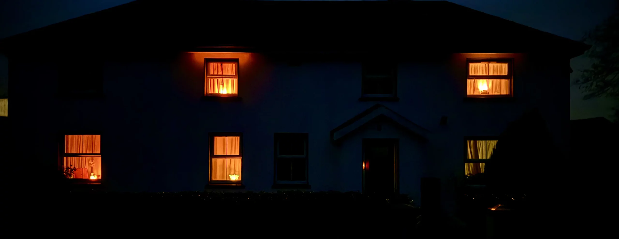 A two-story house at night with warm lights glowing through the windows.